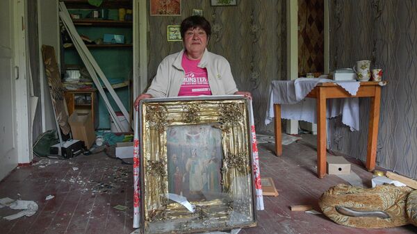 Женщина показывает поврежденную при обстрелах семейную икону в своем разрушенном доме в городе Попасная