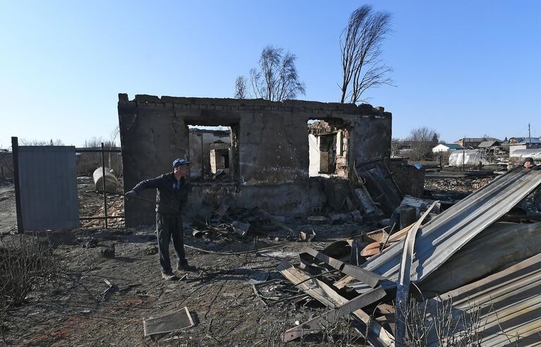 Мужчина собирает металл на пепелище сгоревшего дома для сдачи в пункт приема металлолома в городе Уяре Красноярского края