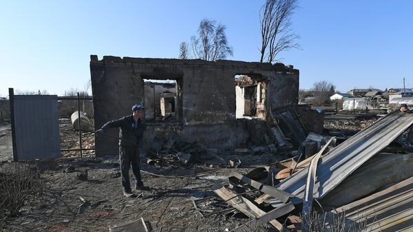 Мужчина собирает металл на пепелище сгоревшего дома для сдачи в пункт приема металлолома в городе Уяре Красноярского края
