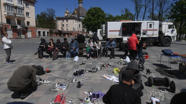Жители заряжают мобильные телефоны и технику от генератора, установленного МЧС РФ на Театральной площади в Мариуполе