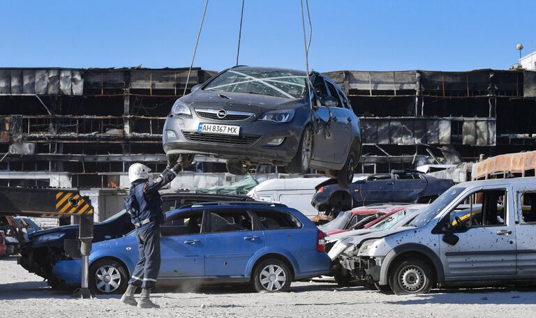 Сотрудник МЧС РФ на стоянке разбитых автомобилей у ТЦ Порт City в Мариуполе