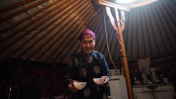Женщина держит чашки чая с молоком в своей юрте, Монголия