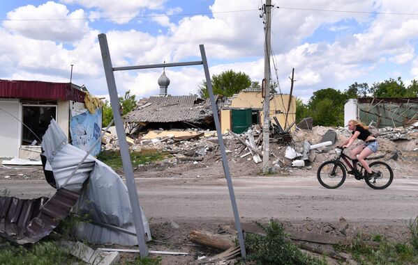Девушка едет на велосипеде мимо разрушенных обстрелами ВСУ домов в освобожденном селе Яцковка