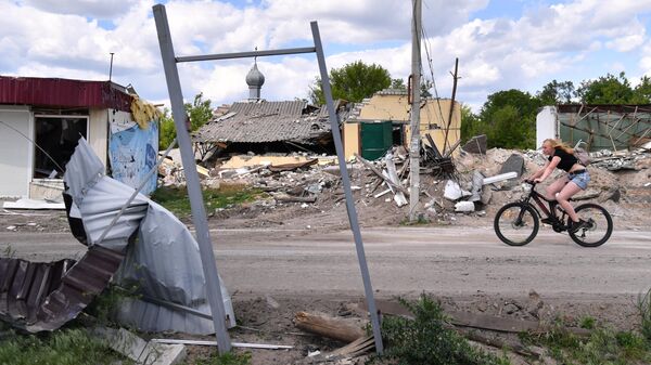 Девушка едет на велосипеде мимо разрушенных обстрелами ВСУ домов в освобожденном селе Яцковка