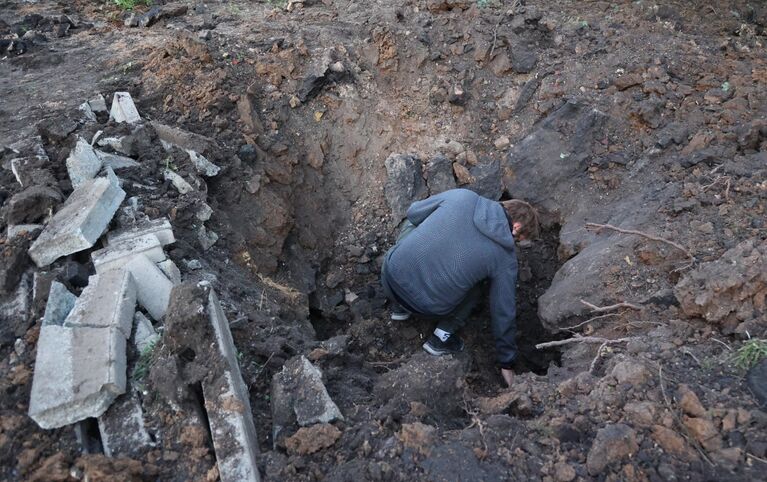 Мужчина осматривает воронку от 155-мм снаряда после обстрела ВСУ жилого сектора в Буденновском районе Донецка