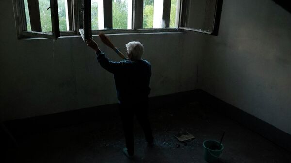 Женщина убирает осколки стекол на лестнице в подъезде жилого дома после обстрела ВСУ 
