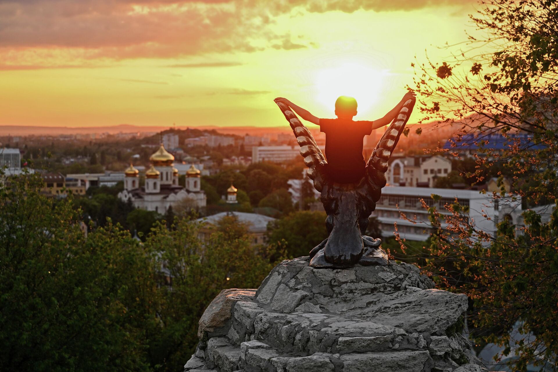 Турист наблюдает за закатом в Пятигорске, сидя на скульптуре орла