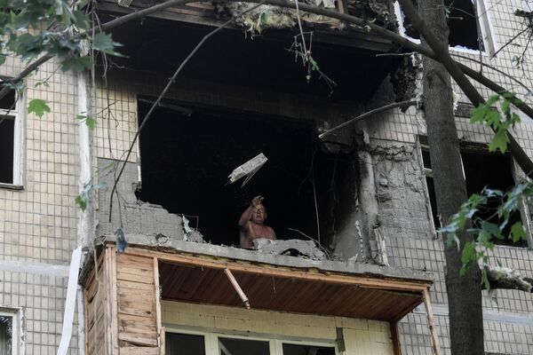 Мужчина выбрасывает разбитое стекло с балкона поврежденного жилого дома в Петровском районе Донецка после обстрелов украинскими войсками