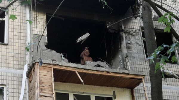 Мужчина выбрасывает разбитое стекло с балкона поврежденного жилого дома в Петровском районе Донецка после обстрелов украинскими войсками