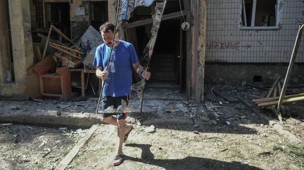 Мужчина выносит разбитое стекло у поврежденного жилого дома в Петровском районе Донецка после обстрелов украинскими войсками