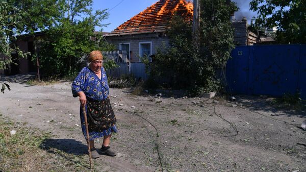 Жительница окраины Северодонецка идет мимо горящего дома, в который попал снаряд при артиллерийском обстреле