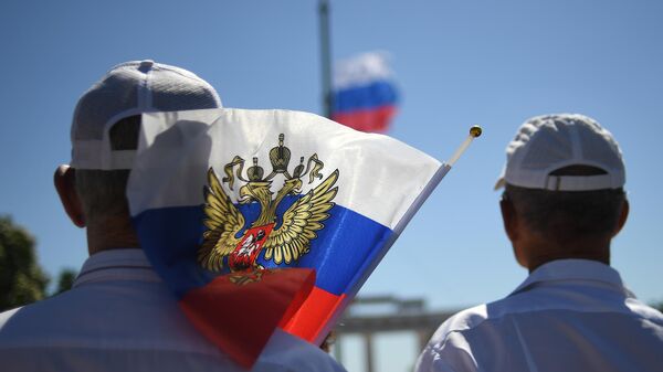 Горожане во время поднятия большого российского флага в честь празднования Дня России на главной площади Мелитополя