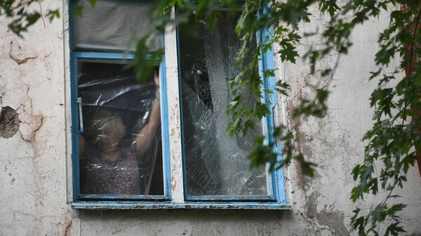 Женщина затягивает полиэтиленовой пленкой окно, разбитое в результате обстрелов  ВСУ Донецка