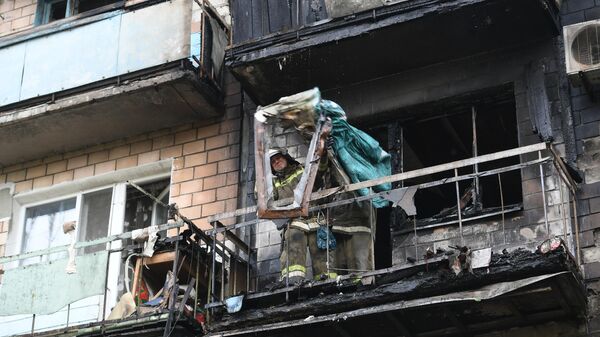 Сотрудник МЧС ДНР выкидывает вещи с балкона дома, сгоревшего в результате обстрелов со стороны ВСУ Донецка