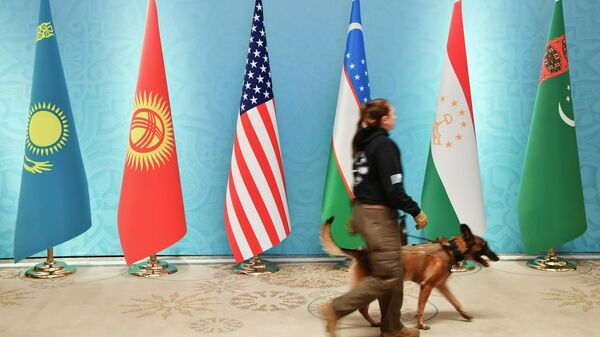 Офицер службы безопасности с собакой-ищейкой проходит мимо национальных флагов: Казахстана, Кыргызстана, США, Узбекистана, Таджикистана и Туркменистана в Ташкенте