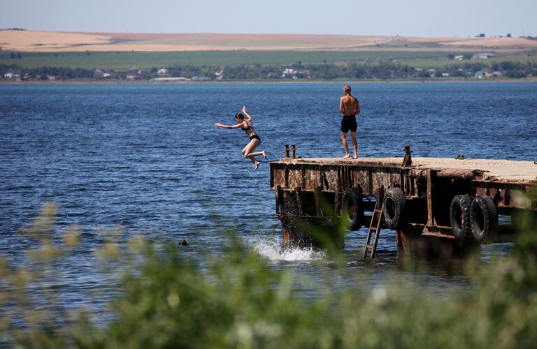 Отдыхающие прыгают с пирса в море на пляже в поселке Сенной в Краснодарском крае