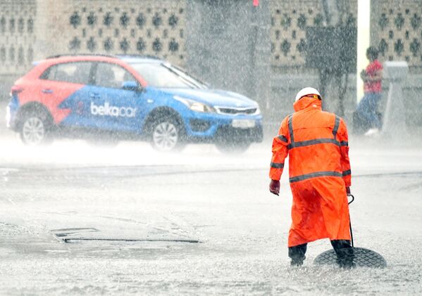 Сотрудник коммунальных служб открывает люк сточной канализации на улице во время дождя в Москве