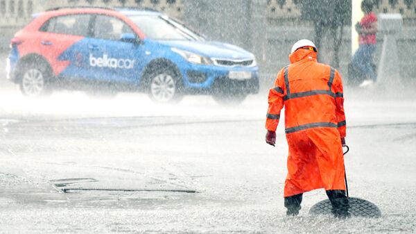 Сотрудник коммунальных служб открывает люк сточной канализации на улице во время дождя в Москве