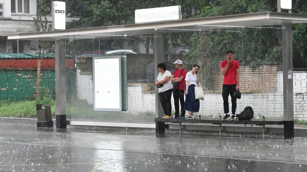 Люди прячутся от дождя на остановке общественного транспорта в Москве