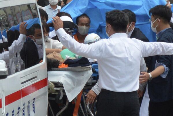 Бывшего премьер-министра Японии Синдзо Абэ (в центре) перевозят в машину скорой помощи возле станции Ямато Сайдайдзи после ранения в городе Нара