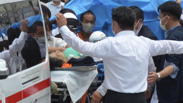 Бывшего премьер-министра Японии Синдзо Абэ (в центре) перевозят в машину скорой помощи возле станции Ямато Сайдайдзи после ранения в городе Нара