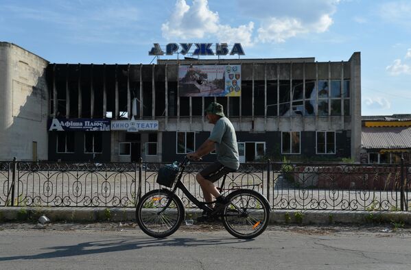 Велосипедист едет мимо разрушенного здания кинотеатра Дружба в Лисичанске
