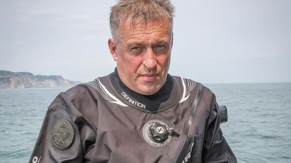 Руководитель проекта 1XPEDITION Сергей Куликов держит найденный деревянный элемент судна