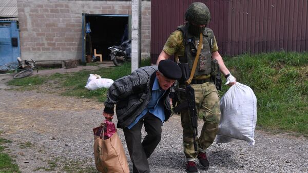 Боец МВД ЛНР помогает пожилому мужчине во время эвакуации в Россию жителей поселка Казачья Лопань в Харьковской области, подвергшийся обстрелу со стороны ВСУ