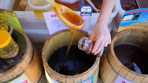 Продавец наливает мед в банку на ярмарке меда в Краснодарском крае.