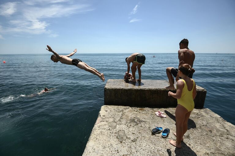 Мужчина прыгает с пирса в море на Массандровском пляже в Ялте