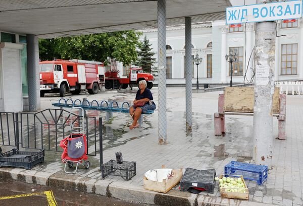 Женщина сидит на остановке общественного транспорта возле здания железнодорожного вокзала в Донецке