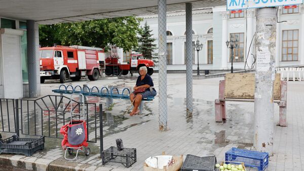 Женщина сидит на остановке общественного транспорта возле здания железнодорожного вокзала в Донецке