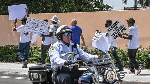 Сотрудник полиции проезжает мимо сторонников экс-президента США Дональда Трампа возле его поместья во Флориде