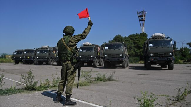 Военнослужащий подает сигналы флажком для проезда военной техники в Мариуполе