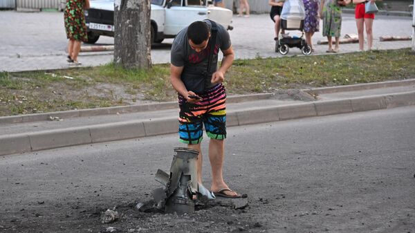 Жители города около неразорвавшегося боеприпаса на месте обстрела Ленинского района Донецка