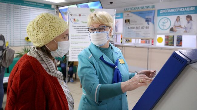 Сотрудница поликлиники помогает посетительнице получить талон к врачу