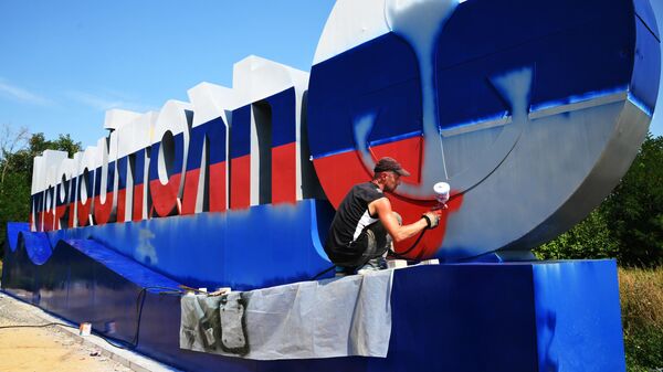Рабочий красит в цвета российского флага стелу на въезде в Мариуполь