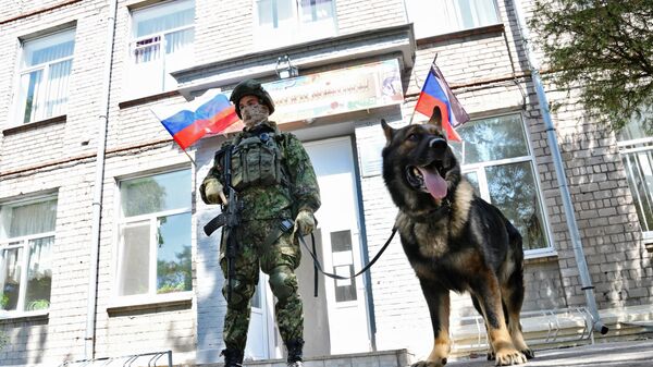 Сапер Международного противоминного центра ВС РФ со служебной собакой у школы №60 в Мариуполе
