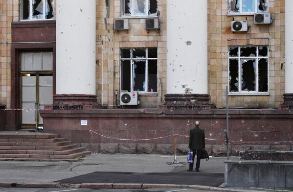 Мужчина возле частично разрушенного здания на одной из улиц в Донецке