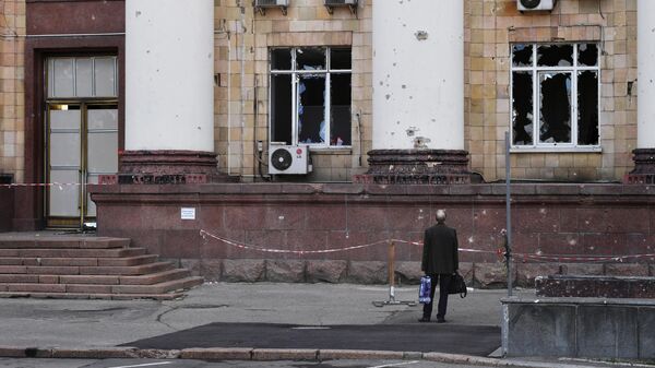 Мужчина возле частично разрушенного здания на одной из улиц в Донецке