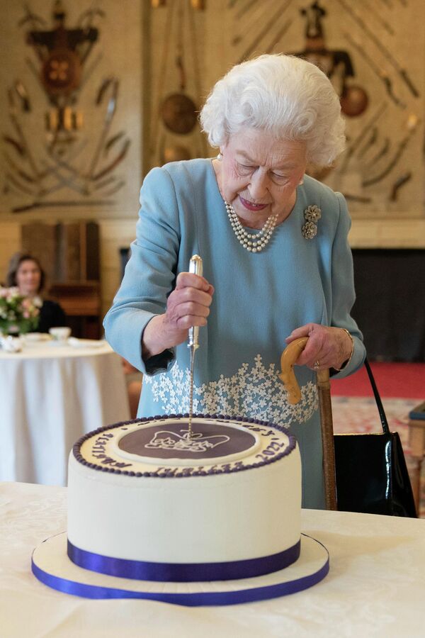 Королева Великобритании Елизавета II разрезает торт, чтобы отпраздновать начало семидесятой годовщины ее правления