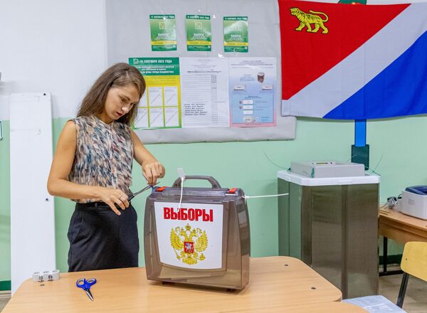 Сотрудница избирательной комиссии во Владивостоке вскрывает переносную урну для дальнейшего подсчета бюллетеней после завершения голосования