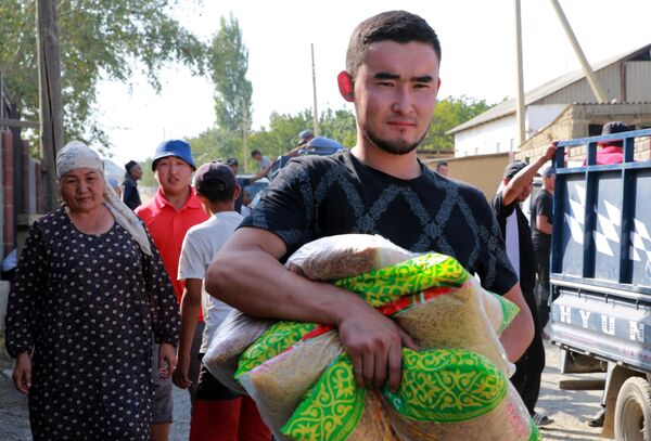 Молодой человек несет пакеты с макаронами во время раздачи гуманитарной помощи беженцам в селе Боз-Адыр в Киргизии
