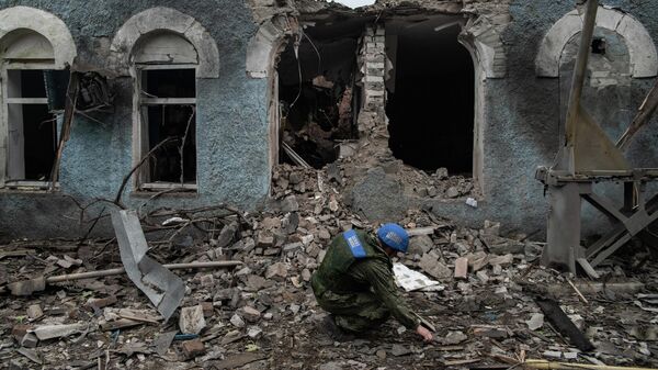 Сотрудник СЦКК собирает фрагменты разорвавшихся снарядов после обстрела со стороны ВСУ