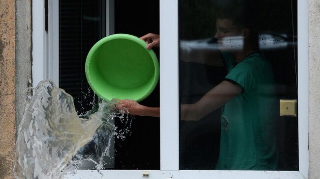 Юноша вычерпывает воду из своей квартиры на затопленной улице