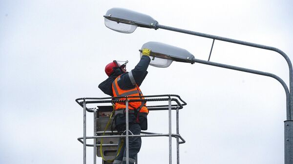 Работник энергетической компании меняет лампы в уличных фонарях