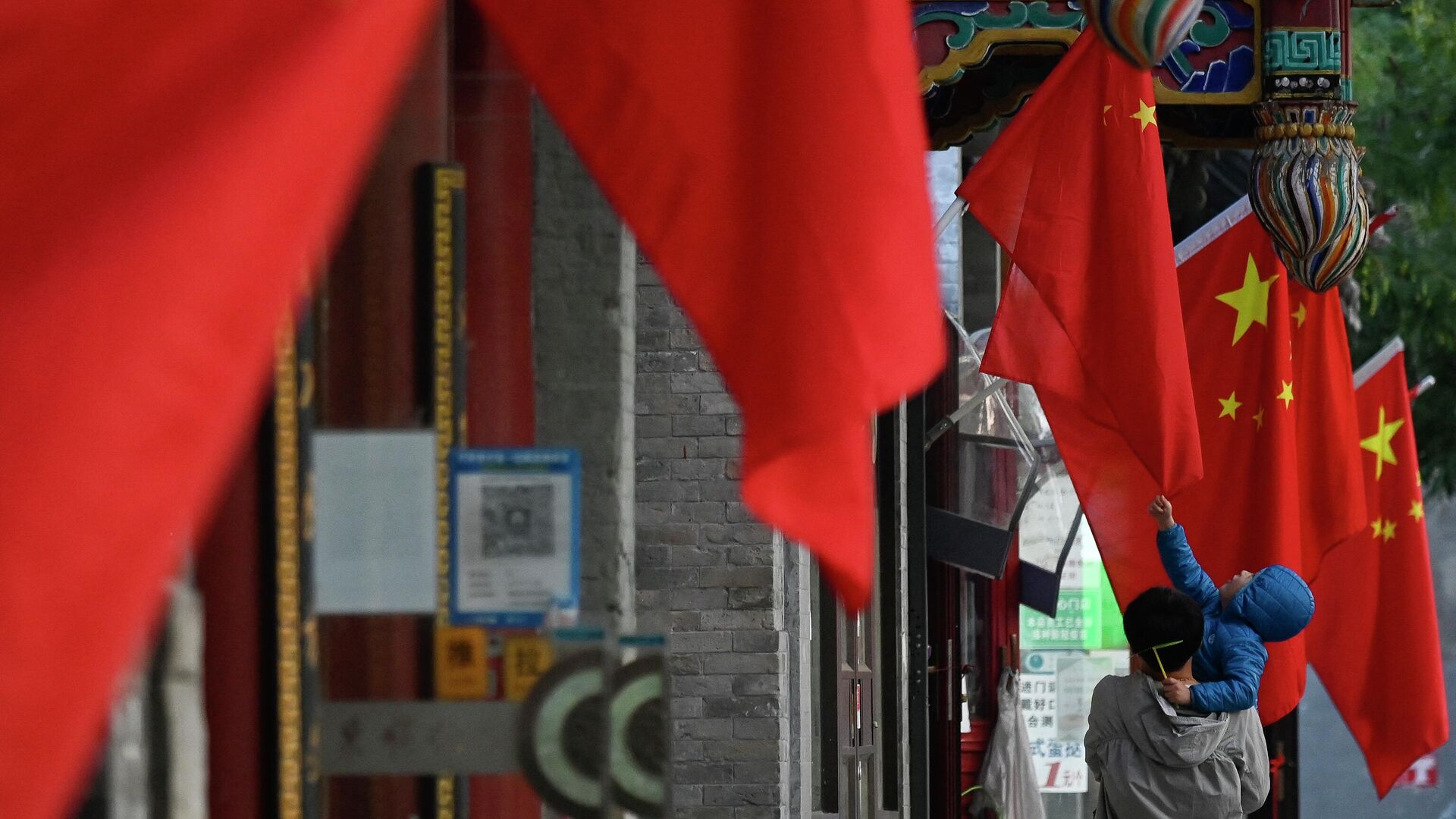 Ребенок касается китайского флага, вывешенного на улице в Пекине, накануне 20-го съезда Коммунистической партии - РИА Новости, 1920, 16.10.2022