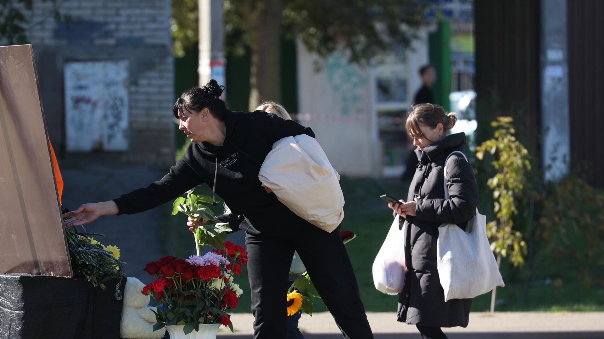 Женщина возлагает цветы к стихийному мемориалу у многоэтажного дома, повреждённого в результате крушения истребителя-бомбардировщика Су-34 в Ейске - РИА Новости, 1920, 18.10.2022