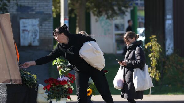 Женщина возлагает цветы к стихийному мемориалу у многоэтажного дома, повреждённого в результате крушения истребителя-бомбардировщика Су-34 в Ейске