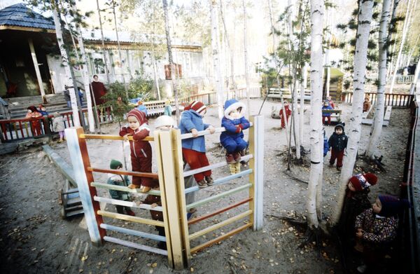 Воспитанники яслей-сада во время прогулки с воспитателем на игровой площадке, находящейся на опушке леса